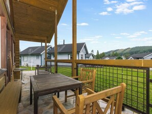 Eine Holzterrasse mit Tisch und Stühlen, mit Blick auf einen umzäunten Garten und Häuser im Hintergrund.