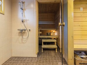 Ein Saunaraum mit Holzboden, einer Dusche, einer Sitzbank und einem Ofen.