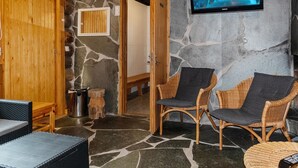 A stone-walled room with a television mounted on the wall, wicker furniture, and a wooden door. - Raahenmaja by Interhome (Inari)