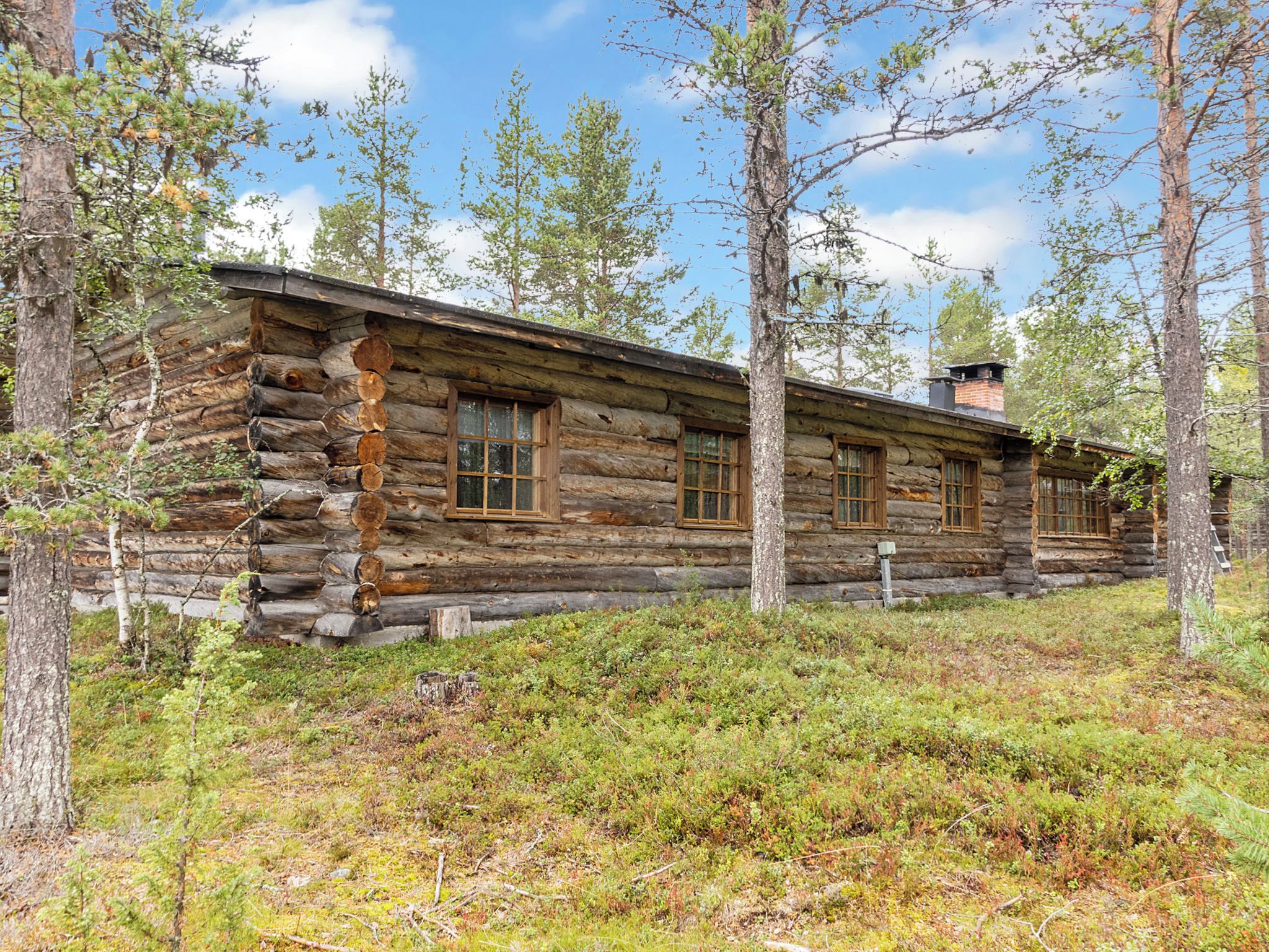 A log cabin with a simple, rustic design, surrounded by a forested area.