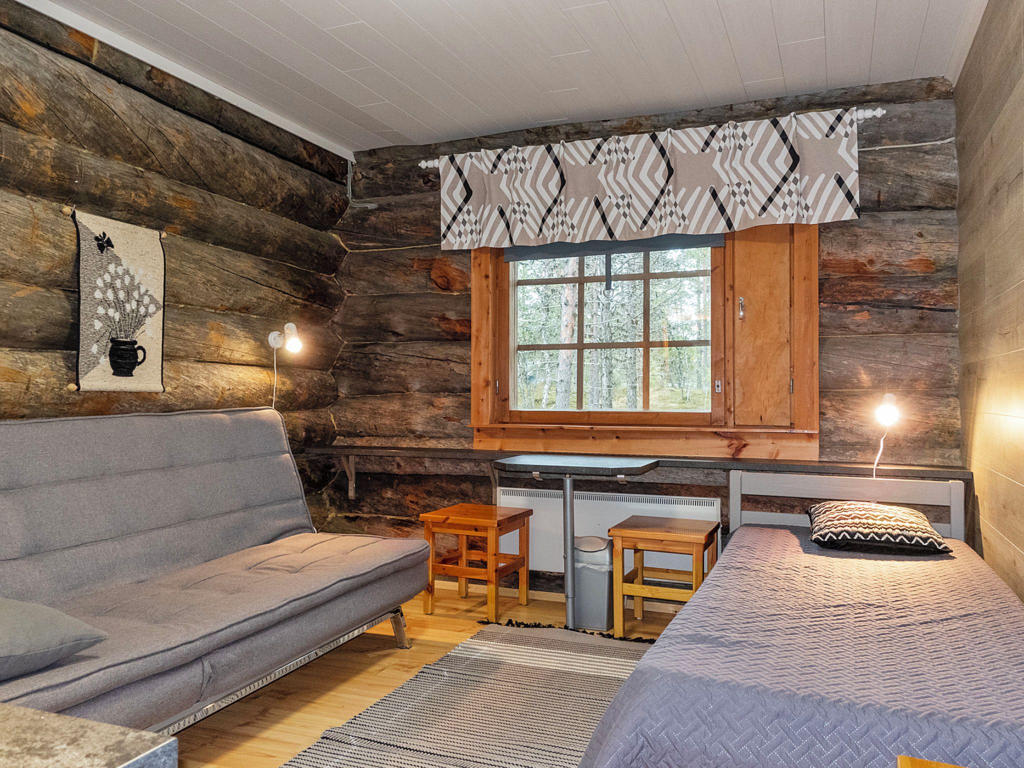 L’intérieur d’une cabane en rondins, avec un canapé, une petite table, un lit et une fenêtre avec des rideaux.