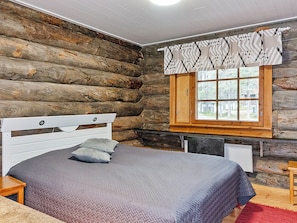 Un dormitorio tipo cabaña de troncos con cabecera de madera, una ventana con cortina adornada y una cama con ropa de cama gris.