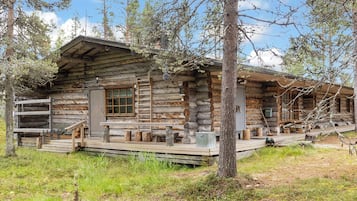 A rustic log cabin with a porch, wooden steps, and a small outdoor seating area.