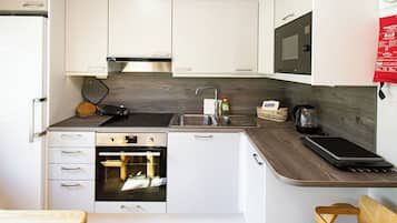 A compact kitchen with white cabinets, a built-in oven, a microwave, and a sink.