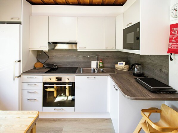 Una cocina compacta con armarios blancos, horno integrado, microondas y pileta.
