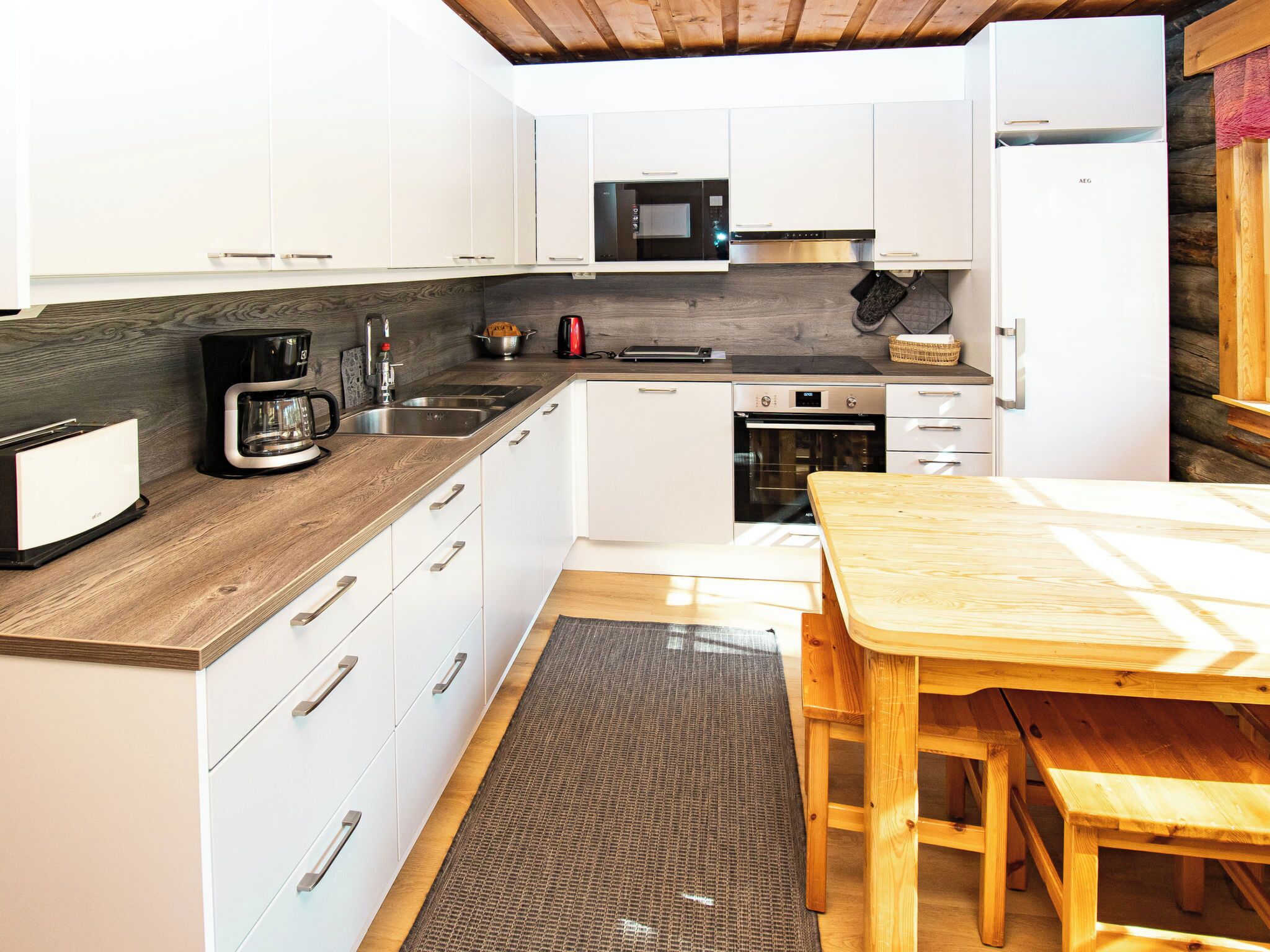 Een moderne keuken met witte kastjes, een magnetron, een oven, een koffiezetapparaat en een houten tafel.