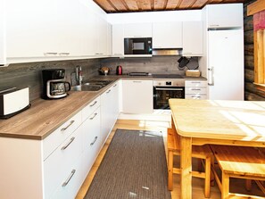 Una cocina moderna con armarios blancos, microondas, horno, cafetera y una mesa de madera.