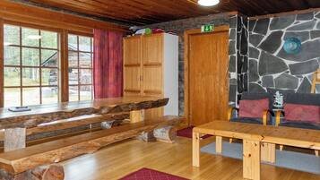 A wooden interior with a stone wall, a wooden bench, a table, and a door marked with an arrow.