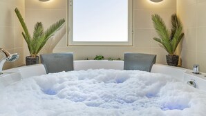A bathroom with a large bathtub filled with bubbles, two potted plants, and a window with a view.
