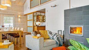 A modern living room with a fireplace, a dining area with a wooden table and chairs, and a cozy seating area with a sofa and cushions.
