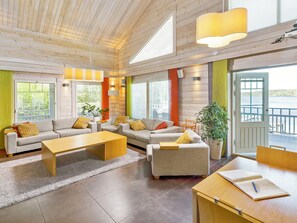 Un soggiorno ampio con soffitto in legno, ampie finestre e vista su un corpo d'acqua.