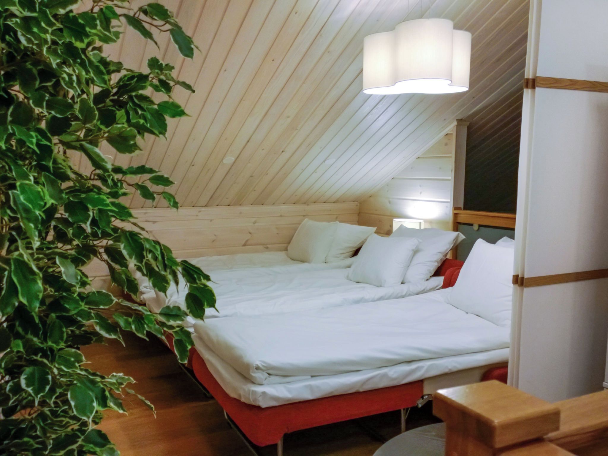 Ett sovrum med ett sluttande tak, en säng med vita sängkläder, ett sängbord och en hängande lampa.