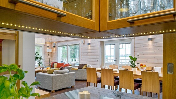 A modern kitchen with wooden cabinets, a dining area with a glass-top table, and a cozy seating area with a sofa and chairs.