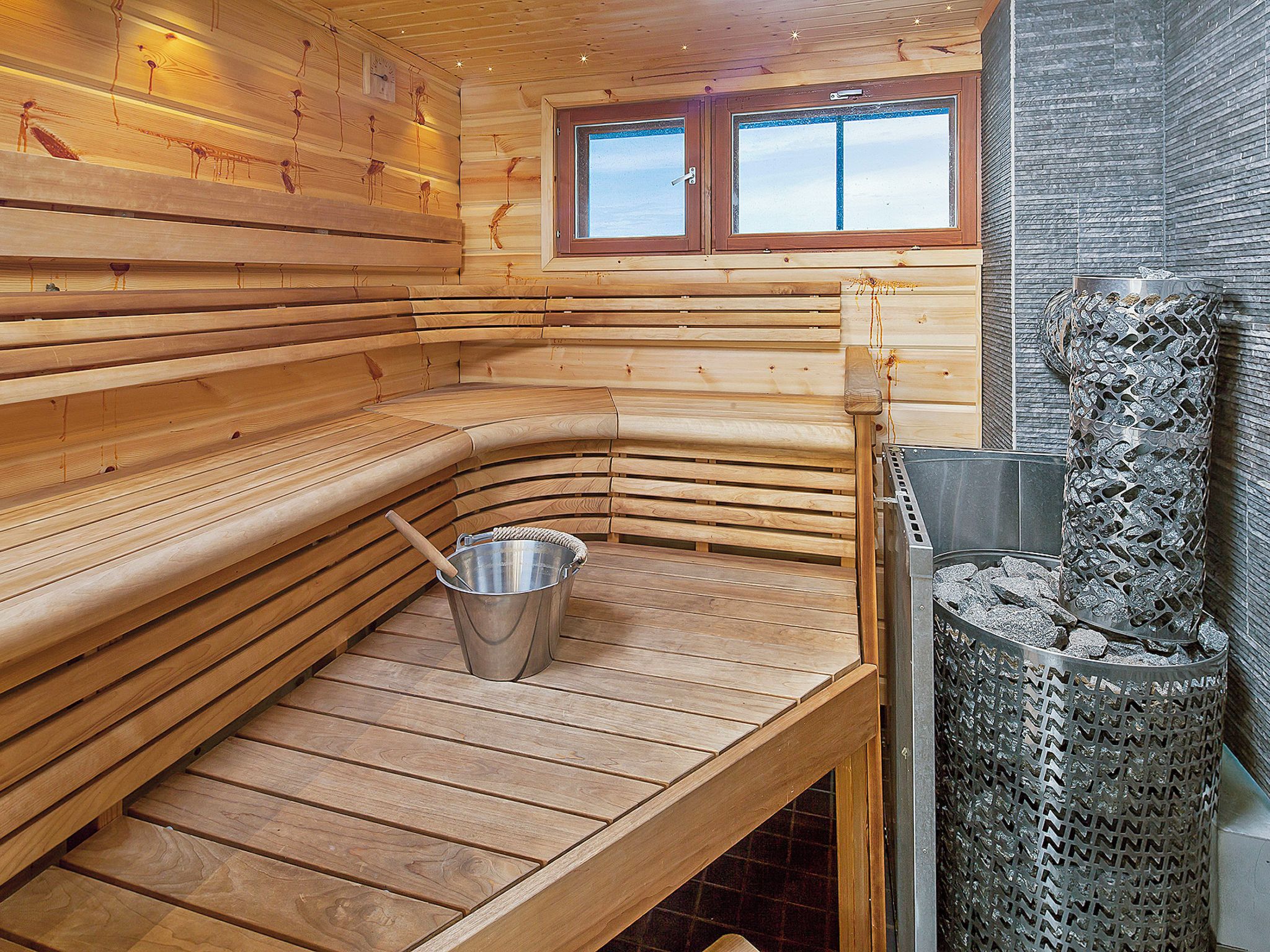 A sauna with wooden benches, a metal bucket, and a textured wall.