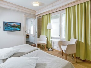 A hotel room with two beds, a small table, two chairs, a desk with a chair, a bathroom, and a painting on the wall.