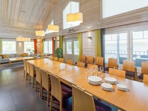 Un comedor amplio con una larga mesa de madera, numerosas sillas y una zona de estar con un sofá y cojines.