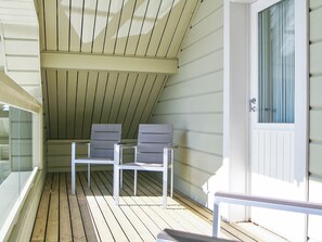 A covered outdoor seating area with two chairs and a bench, wooden floor, and a door with a window. - Riemurahi by Interhome (Pertunmaa)