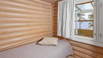 A log cabin room with a bed, a window with curtains, and a view of a lake.