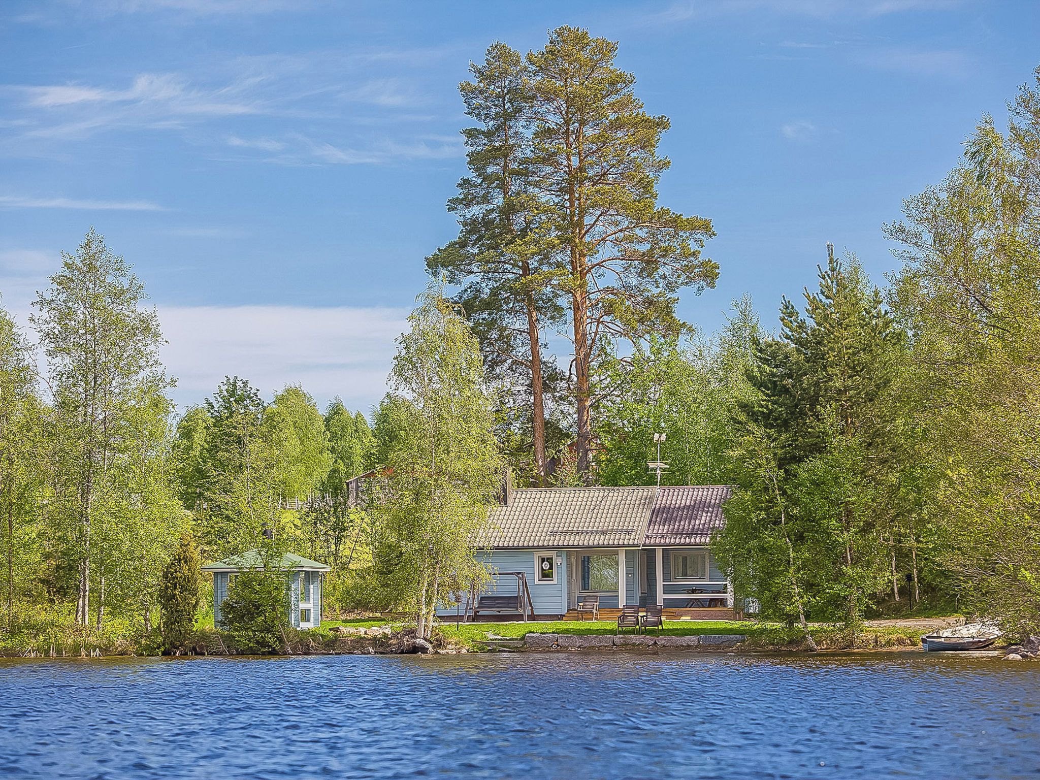 Mökki järven rannalla, jota ympäröivät puut.