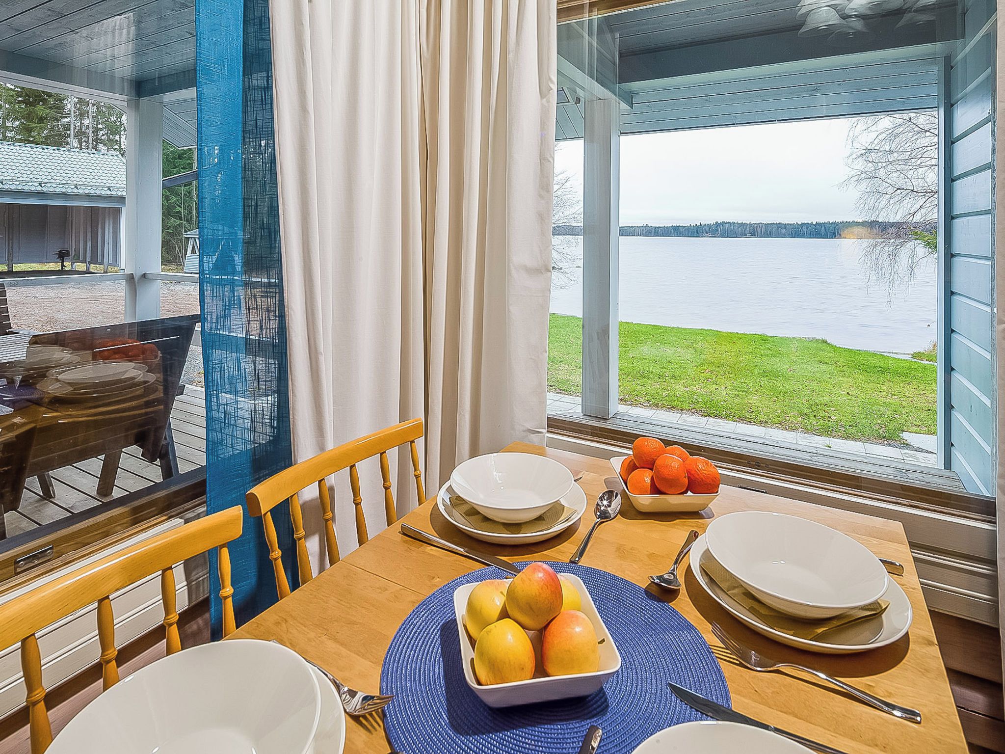 Una mesa de comedor dispuesta con platos, tazones y frutas, con vista a un lago.