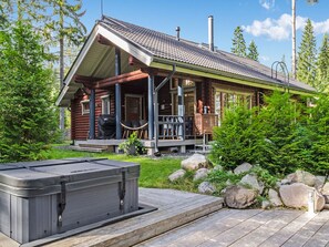 A log cabin with a porch, a hot tub, and a wooden deck.