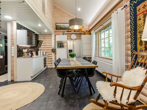 A modern kitchen with a central island, a dining area with a large table and chairs, and a cozy seating area with a chair and a fluffy cushion.