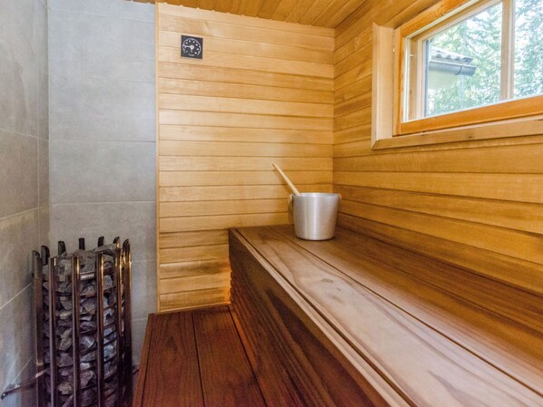 A sauna room with wooden walls, a bench, a metal bucket, and a stone heater.