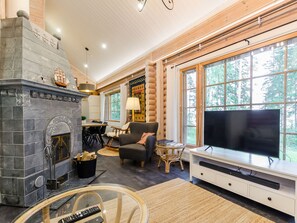 A cozy living room with a stone fireplace, a television, and a large window offering a view of the outdoors.