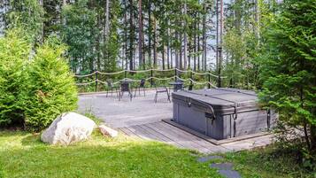 A wooden deck with outdoor seating, surrounded by dense forest and a large rock.