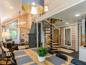 A spacious living area with a wooden interior, a fireplace, a dining table with chairs, and a staircase. - Villa usva by Interhome (Lieksa)