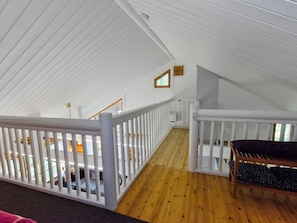 A high-ceilinged interior with white railings and a wooden floor, leading to a balcony area.