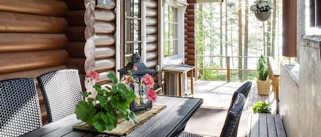 Une cabane en rondins de bois dotée d’un coin repas avec une table et des chaises, d’une jardinière suspendue et d’une vue sur la forêt.