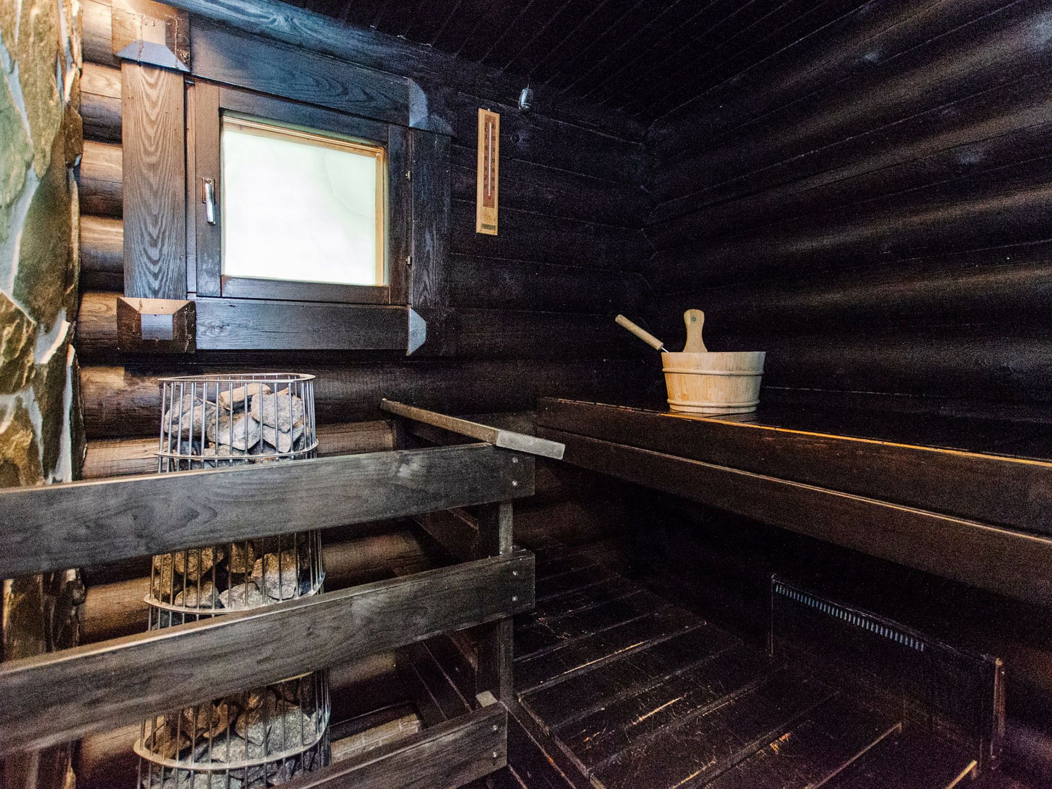 Ein Blockhaus-Innenraum mit einer hölzernen Bank, einem Kamin mit einem Metallgitter und einer Steinwand.