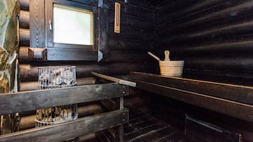 A log cabin interior with a wooden bench, a fireplace with a metal grate, and a stone wall.