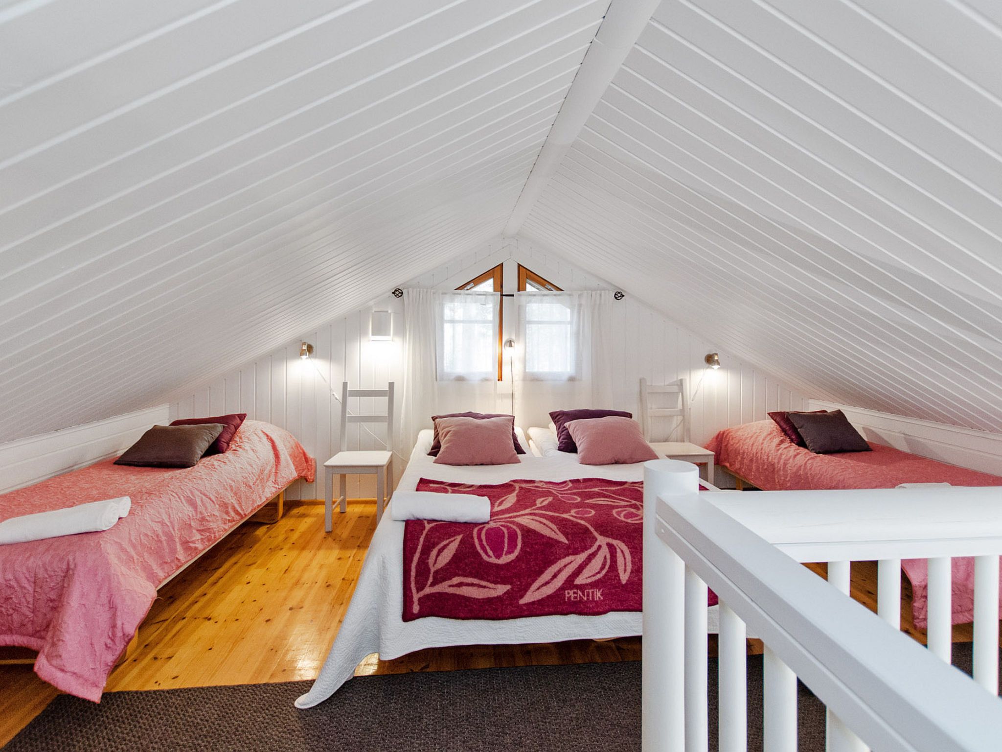 Ein gemütliches Schlafzimmer im Dachgeschoss mit zwei Einzelbetten, einem Doppelbett in der Mitte und einem weißen Geländer.