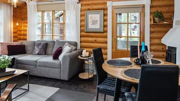 A cozy log cabin interior with a grey sofa, a dining table with chairs, and a fireplace.