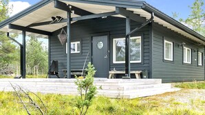 A dark-colored cabin with a covered porch, a door, and windows.