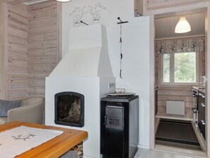 L’intérieur d’un chalet accueillant, avec un mur lambrissé, une cheminée, un petit coin cuisine et une table à manger.