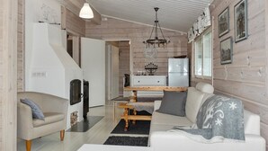 A cozy living room with a sofa, a coffee table, and a fireplace. There is a kitchen area with a refrigerator and a dining table.