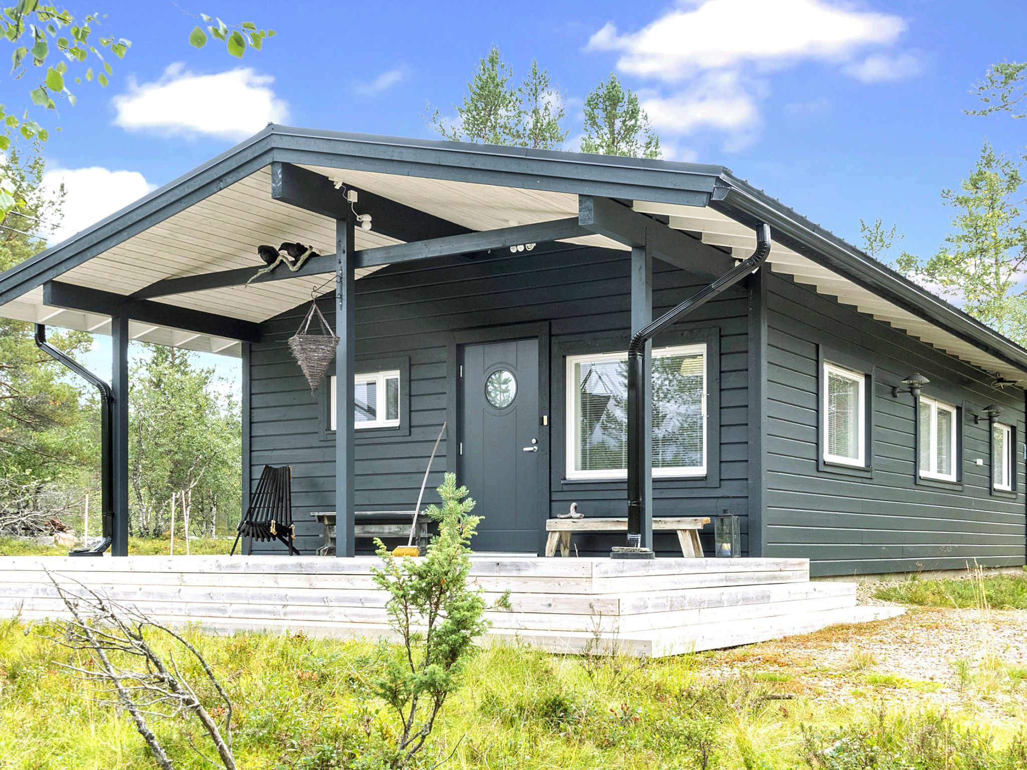A dark-colored cabin with a covered porch, a front door, and a window.
