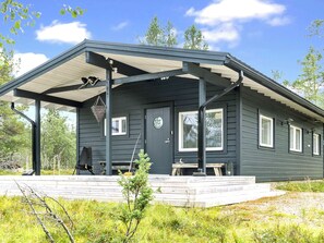 Une cabane aux couleurs sombres, dotée d’un porche abrité, d’une porte d’entrée et d’une fenêtre.