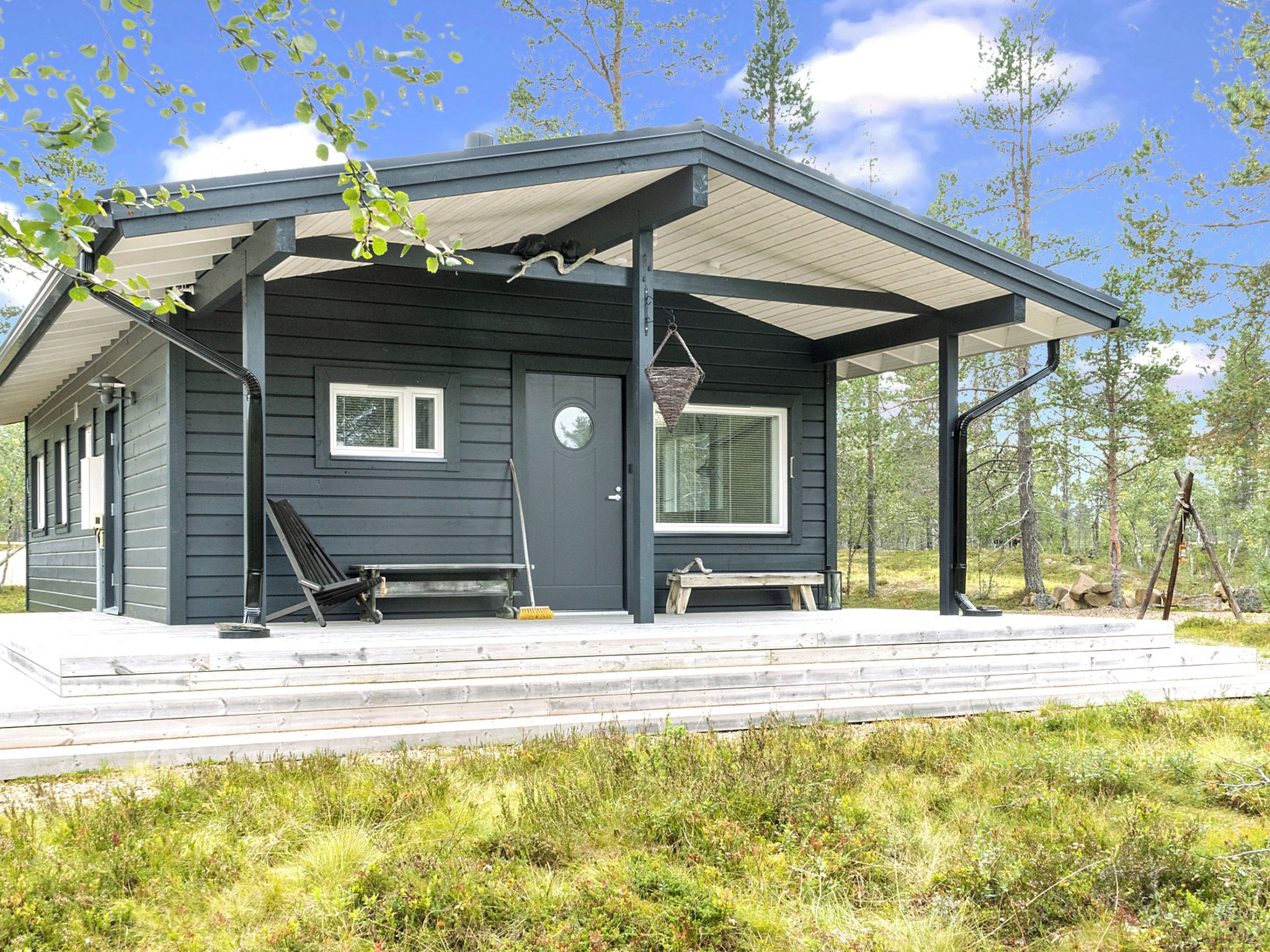Une cabane moderne dotée d’un porche abrité, d’un banc et d’un balai.
