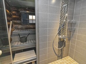 A shower area with a tiled wall, a metal showerhead, and a metal rack. - Agenttimajat 2 by Interhome (Kuusamo)