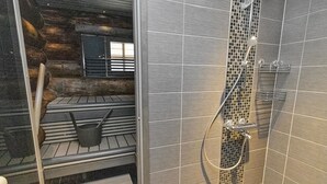 A shower area with a glass door, tiled walls, and a metal shelf with a bucket. - Agenttimajat 2 by Interhome (Kuusamo)