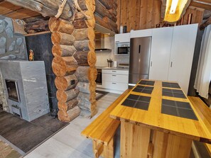 A rustic kitchen with a stone wall, wooden logs, a wooden table with black placemats, and modern appliances.