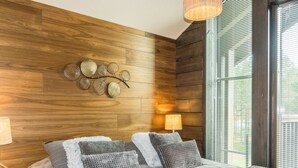 A bedroom with a wooden wall, a bed with patterned bedding, and a window with blinds. - Levi platinum 2 b 6 by Interhome (Kittilä)