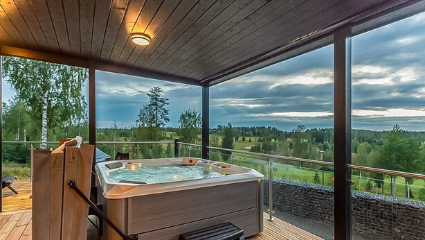 Un bain à remous sur une terrasse en bois, avec vue sur une forêt et un ciel nuageux.