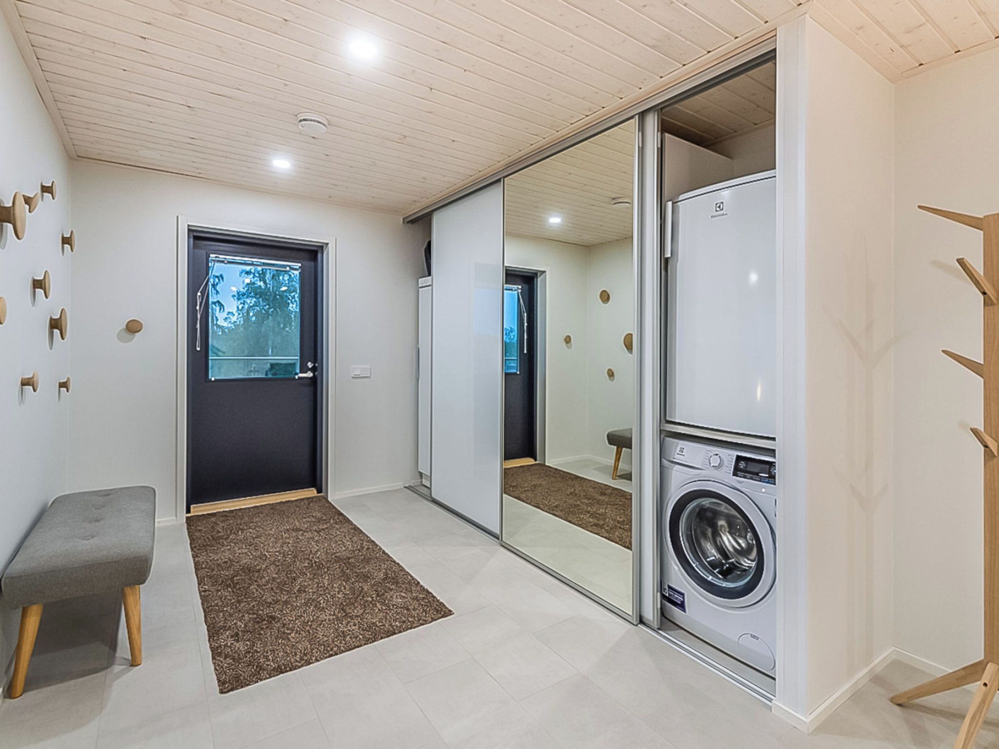 A laundry room with a washing machine, a bench, and a sliding door leading to another room.