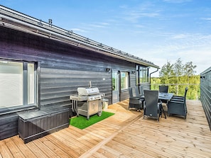A modern outdoor deck with a barbecue grill, dining chairs, and a table.