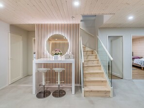 A modern interior with a wooden staircase, a white counter with stools, and a round mirror.